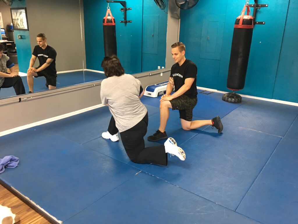Fitness coach in Mission Viejo shows woman in black pants how to perform stretch on mat