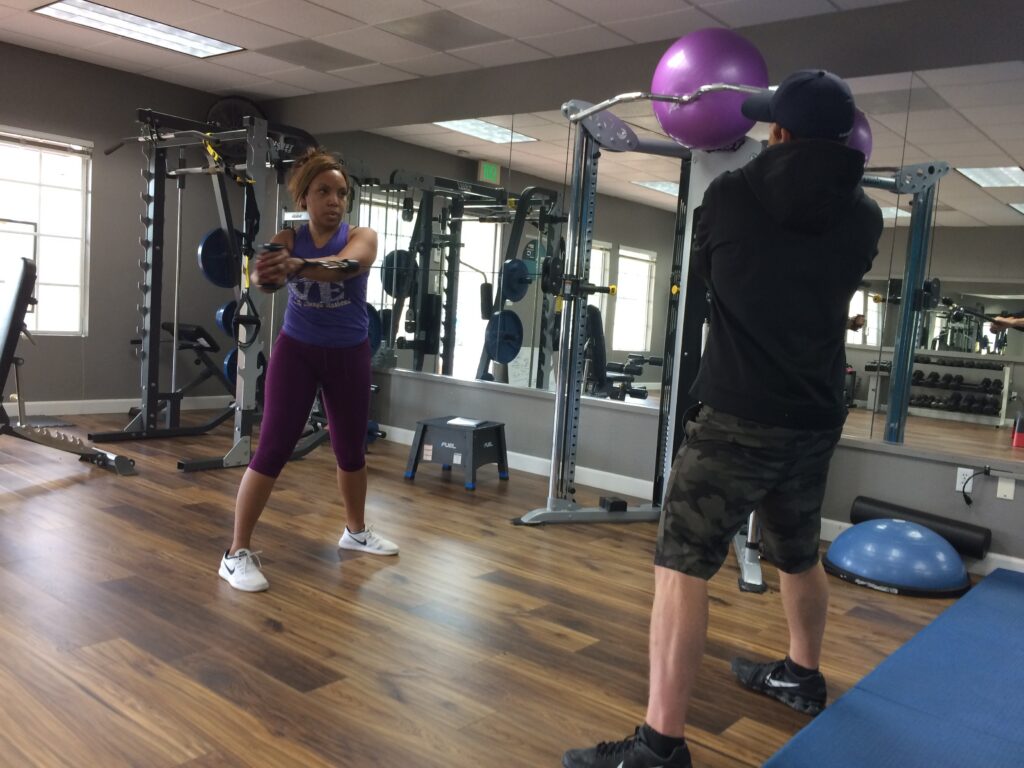 fitness coach in Mission viejo with black shirt helping client in white shoes and striped shorts