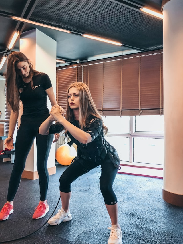 Mission Viejo personal trainer in black gear helps young woman with blonde ahir do squats